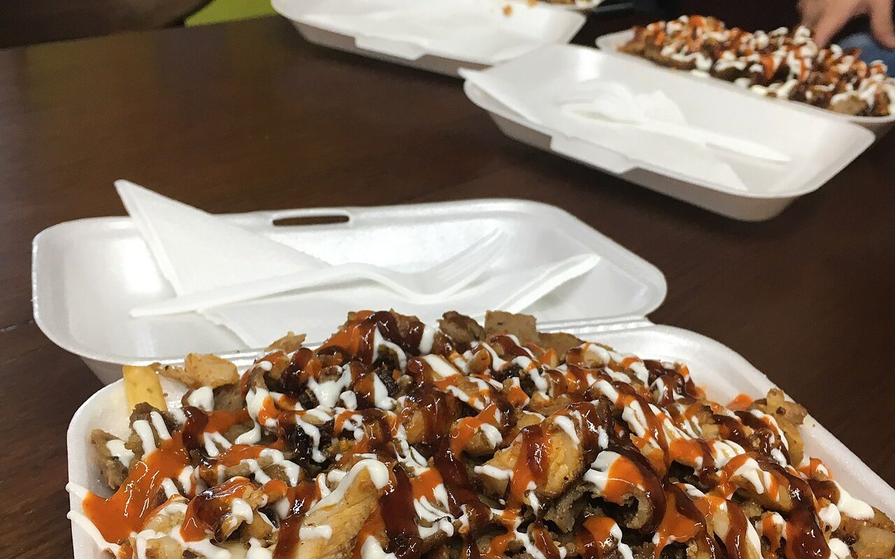 Takeaway boxes of chips topped with meat, garlic sauce and chilli sauce