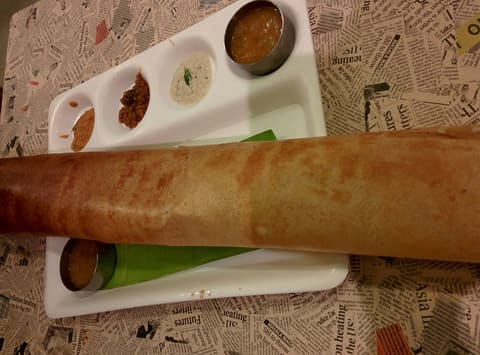 Long rolled paper dosa on a compartment tray with sambar and chutneys