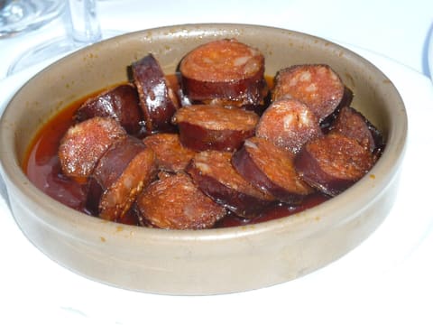Thick slices of cooked reddish chorizo in a tan bowl with orange cooking oil