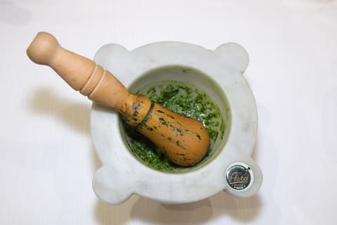 Coarse green basil pesto in a white marble mortar with a wooden pestle