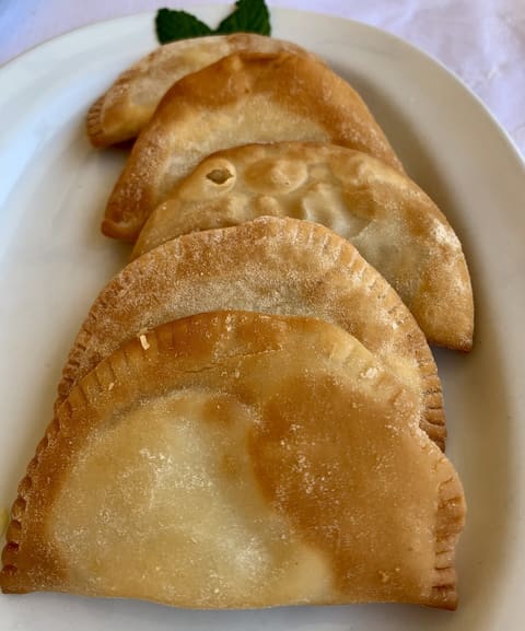 Fried crescent pies with crimped edges on a white plate, photographed in Almyrida, Crete