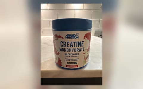 A tub of Applied Nutrition Creatine Monohydrate, cherry and apple flavour, on a kitchen counter