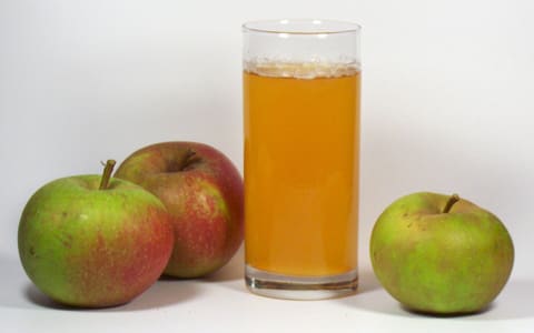 A glass of apple juice beside apples, a typical malic-acid drink