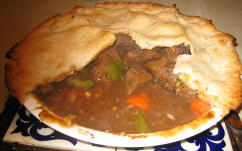 A homemade meat pie cut open to show the meat and vegetable filling