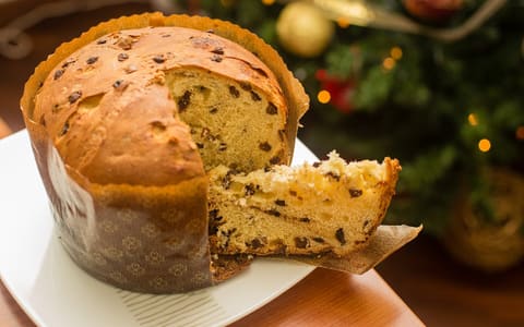 A panettone in its paper case, with a wedge cut out to show the fruit inside