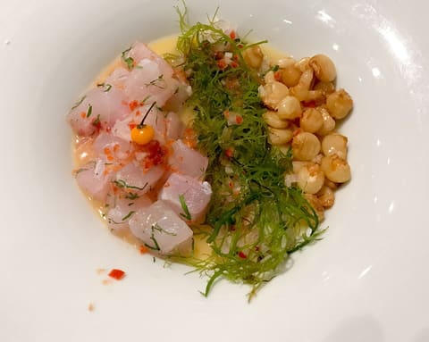 Peruvian ceviche in a white bowl: cubed fish in citrus marinade with seaweed threads and toasted corn