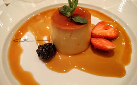 A turned-out panna cotta with caramel sauce, berries and mint
