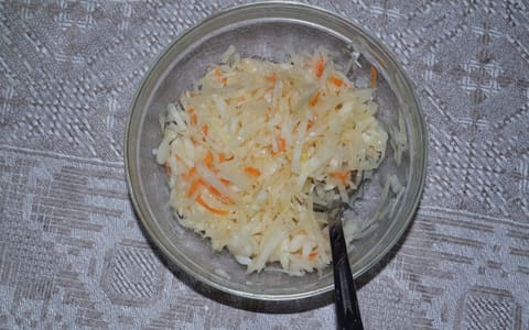 A glass bowl of sauerkraut with shredded carrot