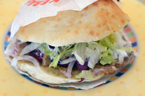 German-style döner kebab in round toasted flatbread with lettuce, red cabbage and white sauce, on a plate