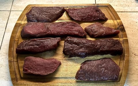 Raw venison steaks laid out on a wooden chopping board