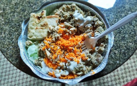 A foil platter of chopped chicken over rice with white sauce, lettuce and pita