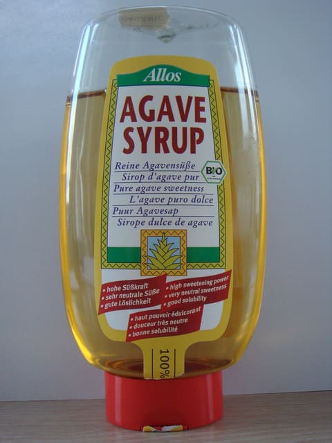 Commercial squeeze bottle labelled agave syrup, filled with amber liquid, standing on a red cap
