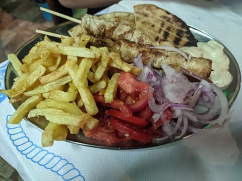Greek chicken souvlaki merida: grilled meat cubes on wooden skewers with pita, fries, tomato, onion and tzatziki